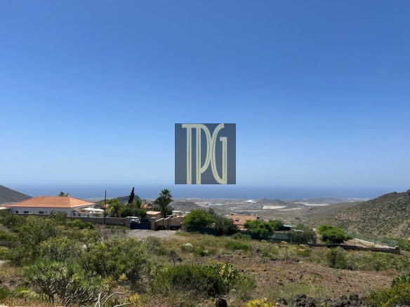 Coastal hillside village with houses, shrubs, and a clear blue sky overlooking the sea on the horizon