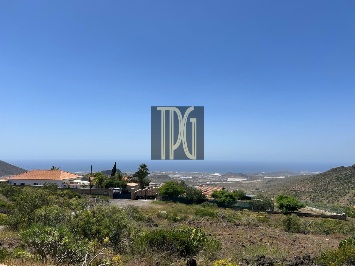 Coastal hillside village with houses, shrubs, and a clear blue sky overlooking the sea on the horizon