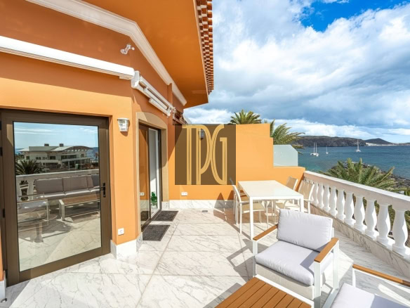 Orange-walled terrace with white outdoor furniture overlooking the sea and palm trees.] ,