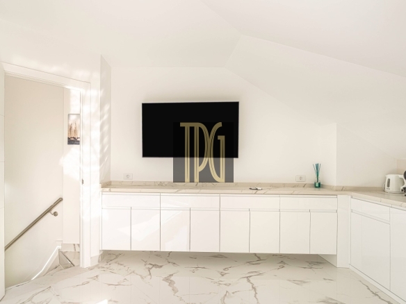 Minimal white kitchen with a mounted TV on a white wall above marble countertops and glossy cabinets