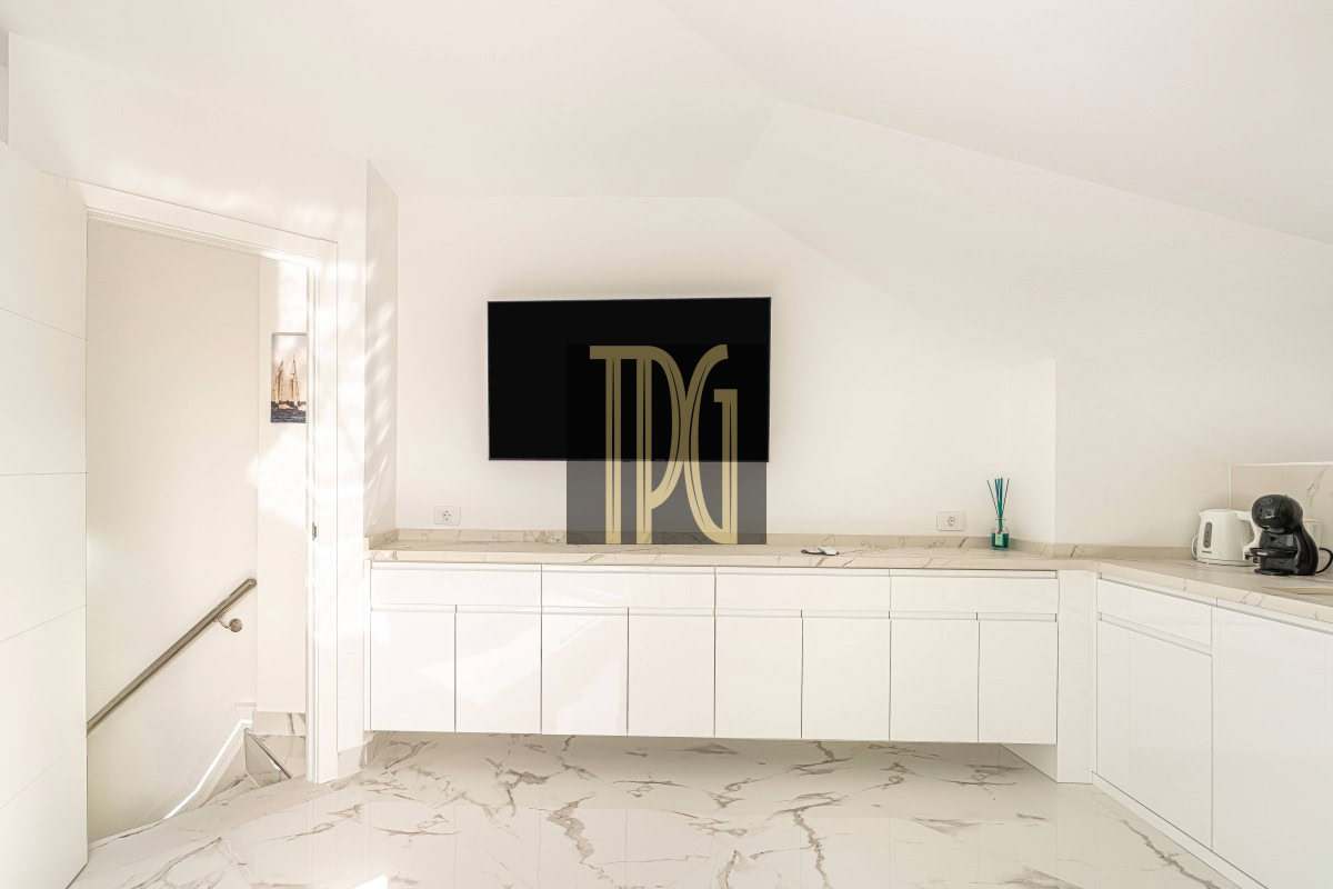 Minimal white kitchen with a mounted TV on a white wall above marble countertops and glossy cabinets