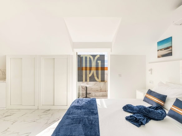 Bright white bedroom with marble floor, a large bed dressed in white with blue throw and pillows, and a glass door to a balcony.