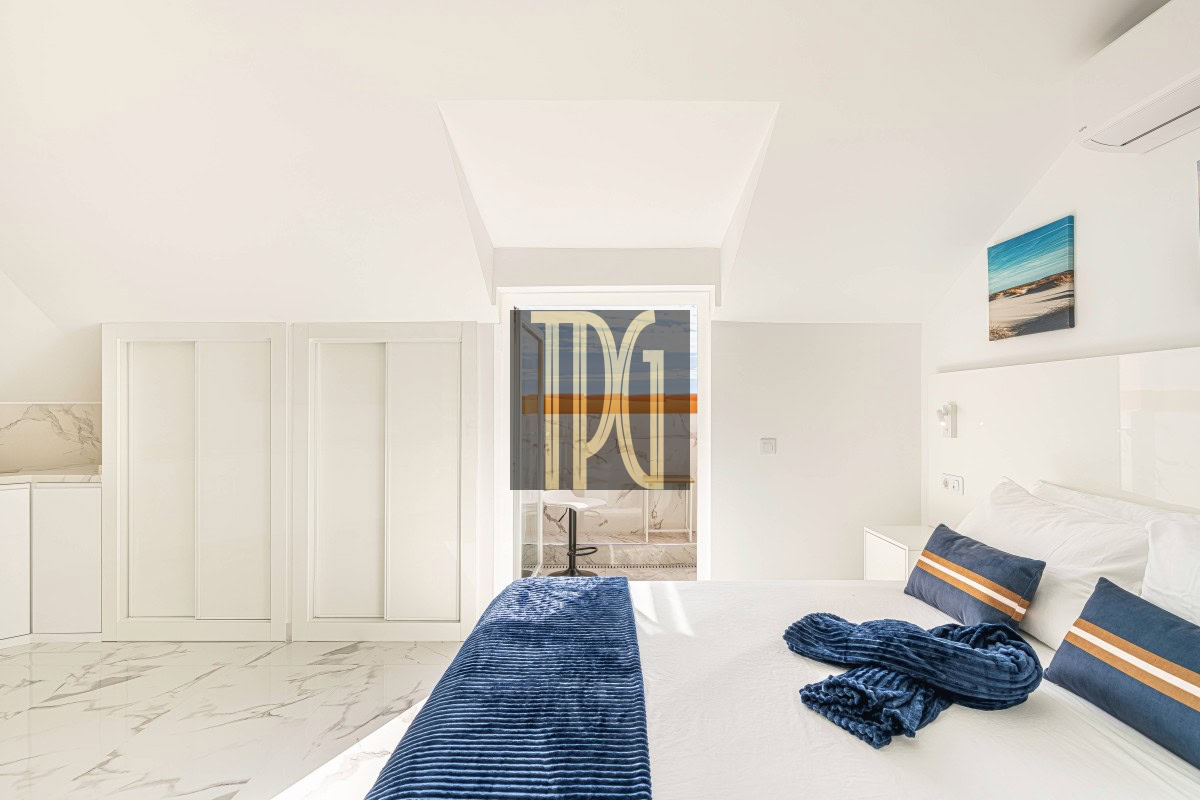 Bright white bedroom with marble floor, a large bed dressed in white with blue throw and pillows, and a glass door to a balcony.