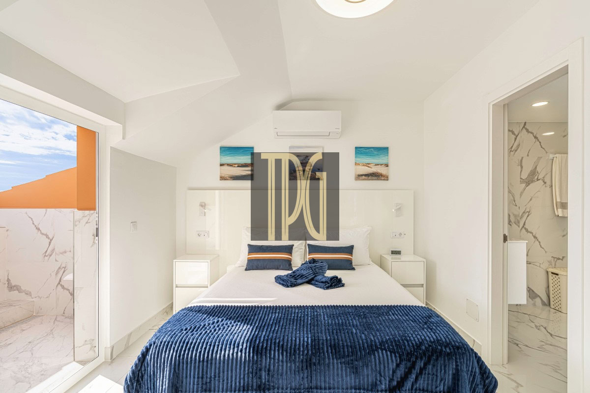 Bright modern bedroom with white walls, two nightstands, and a bed dressed in a navy blue throw blanket and pillows, plus a balcony door to the outside.