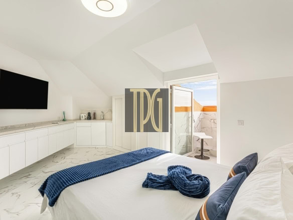 Bright minimalist bedroom with a white bed, blue throw and pillows, and a balcony door open to a marble terrace.