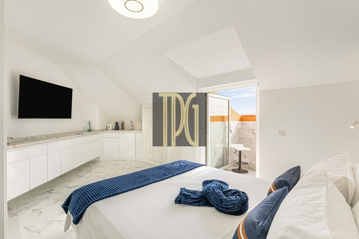 Bright minimalist bedroom with a white bed, blue throw and pillows, and a balcony door open to a marble terrace.