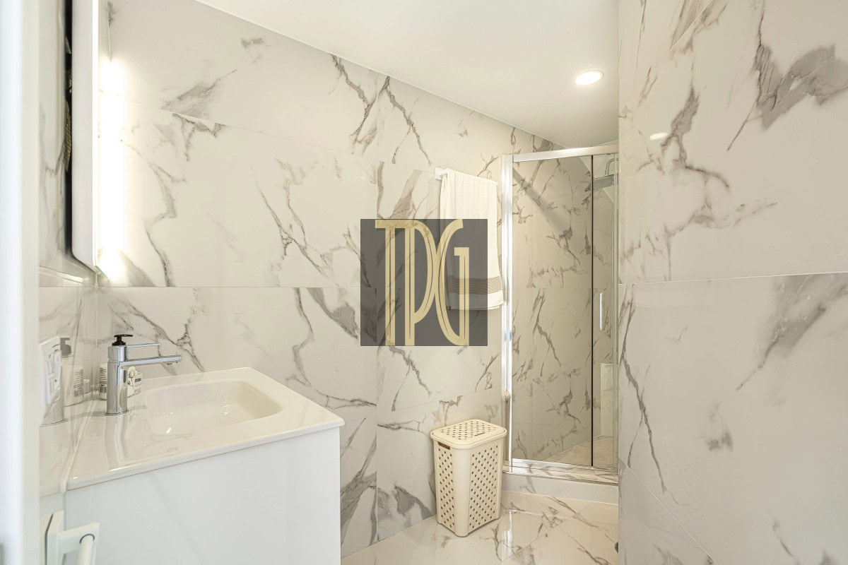Modern white marble bathroom with a sink, vanity, and glass-enclosed shower in a bright, minimalist space.