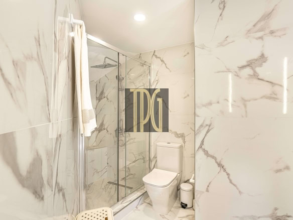 Modern marble-tiled bathroom with a glass shower enclosure, white toilet, and a towel on a rack.
