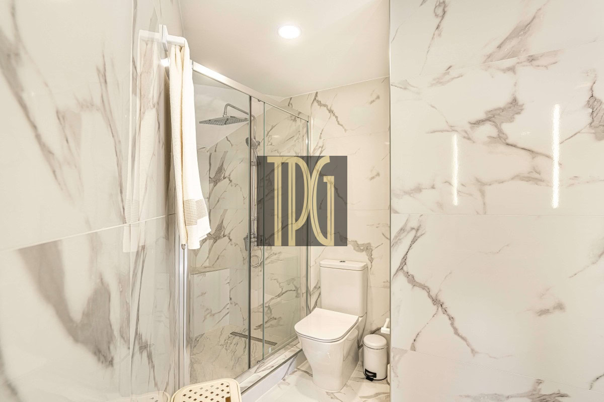 Modern marble-tiled bathroom with a glass shower enclosure, white toilet, and a towel on a rack.