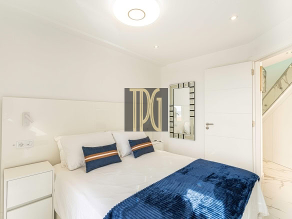 Bright, minimal white bedroom with a neatly made bed, white bedding, and blue accent pillows and throw.