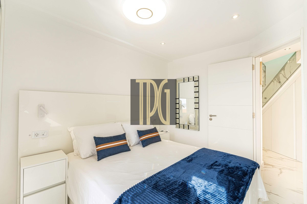 Bright, minimal white bedroom with a neatly made bed, white bedding, and blue accent pillows and throw.