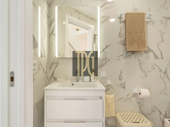 Small modern bathroom with white vanity, backlit rectangular mirror, and marble walls.