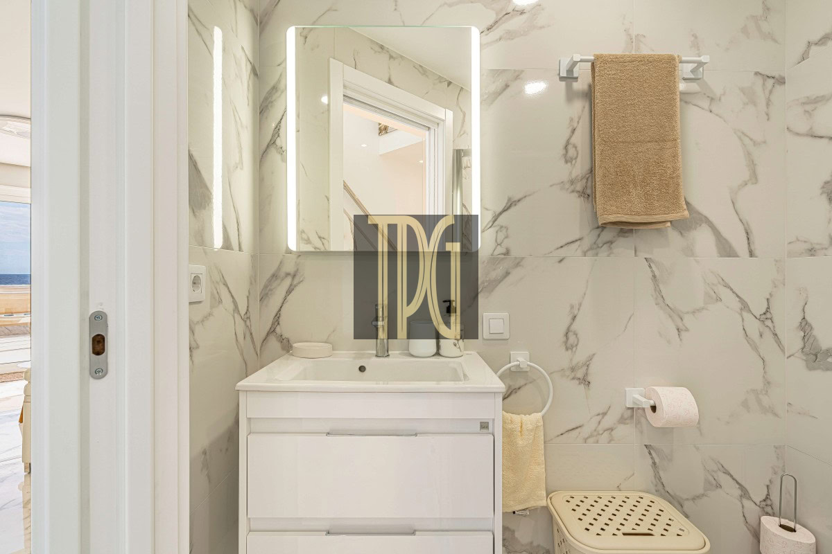 Small modern bathroom with white vanity, backlit rectangular mirror, and marble walls.