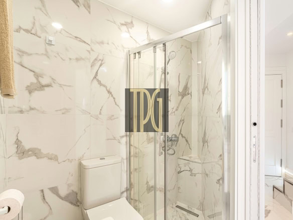 Modern marble-tiled bathroom with a glass shower enclosure and a toilet nearby.