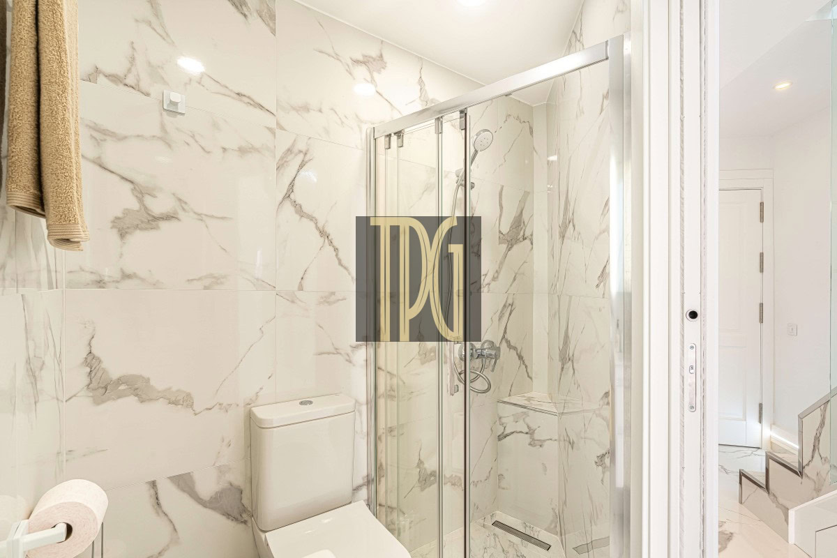 Modern marble-tiled bathroom with a glass shower enclosure and a toilet nearby.
