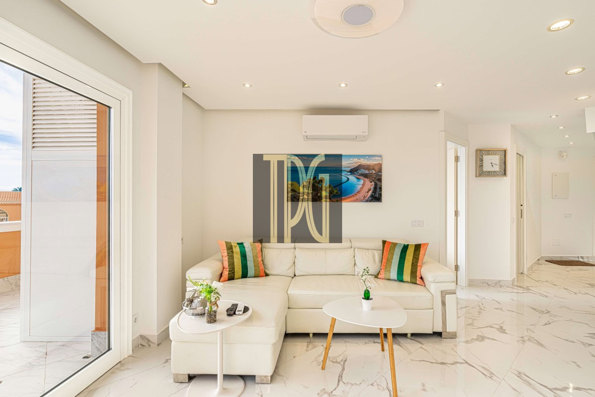 Bright living room with a white sectional sofa, colorful striped cushions, and a marble floor near a sliding glass door to a balcony.