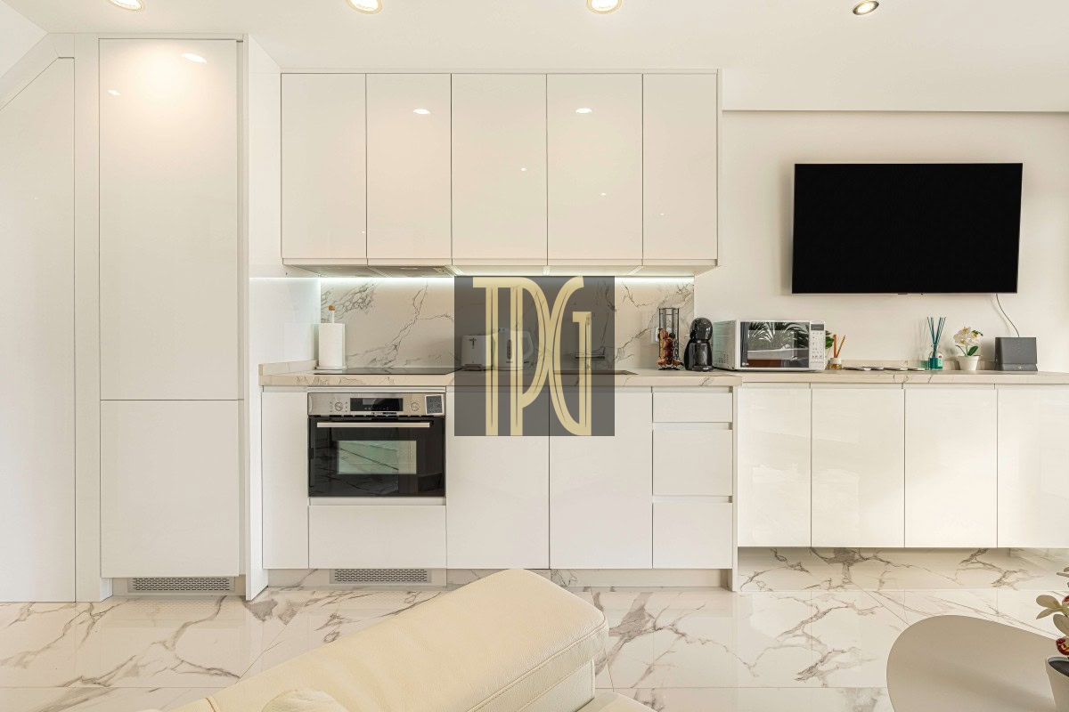 White contemporary kitchen with glossy cabinets, marble backsplash, and built-in oven under a stovetop.