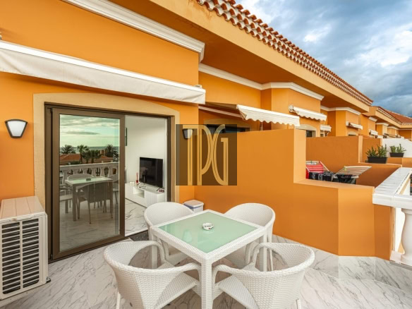Orange balcony with a glass-top table and four white wicker chairs, sliding glass door, and an outdoor air conditioner on a marble floor.