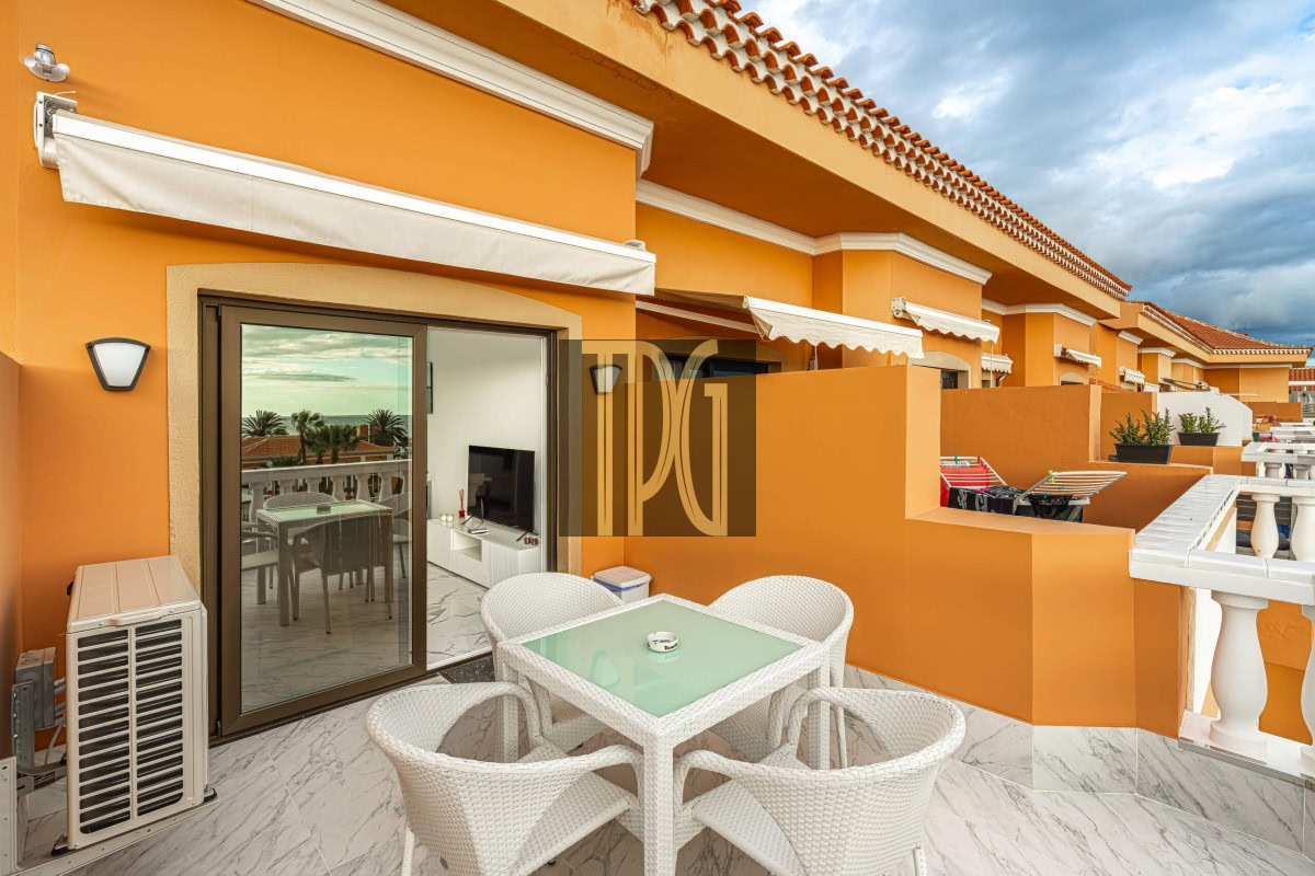 Orange balcony with a glass-top table and four white wicker chairs, sliding glass door, and an outdoor air conditioner on a marble floor.