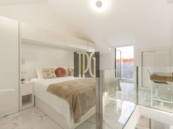Bright white hotel bedroom with a king bed, beige throw, floral cushions, and a glass railing by the stairs.