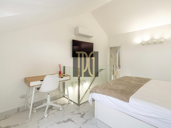 Modern white bedroom with a bed, glass railing, and a small wooden desk with a white chair