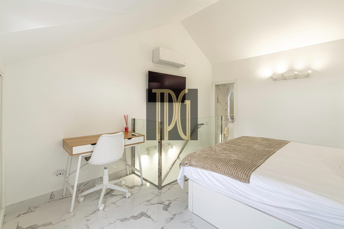 Modern white bedroom with a bed, glass railing, and a small wooden desk with a white chair