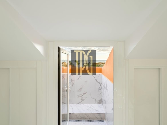 Open doorway revealing a marble-tiled balcony with an orange wall and ocean view beyond.