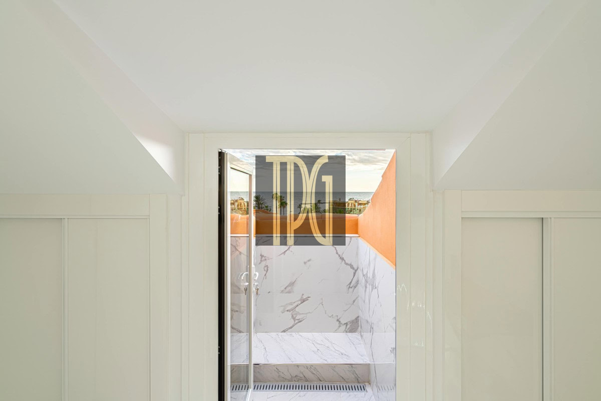 Open doorway revealing a marble-tiled balcony with an orange wall and ocean view beyond.