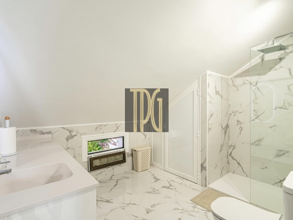 Bright marble bathroom with glass shower, white vanity, and small window.