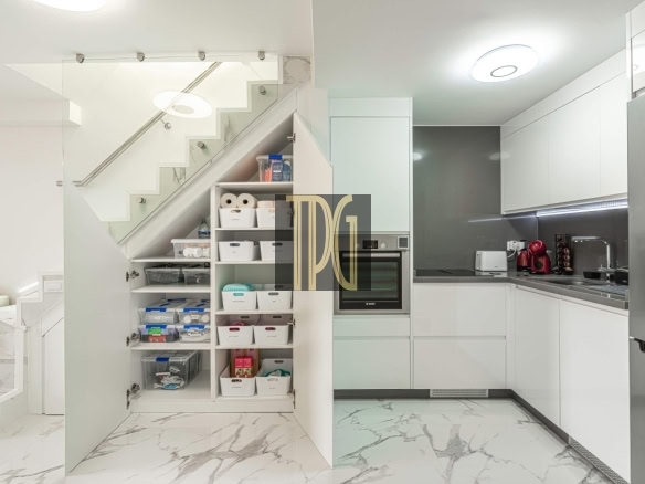 Bright, modern kitchen with white cabinets, marble floors, and a pantry under the staircase with organized bins and shelves.