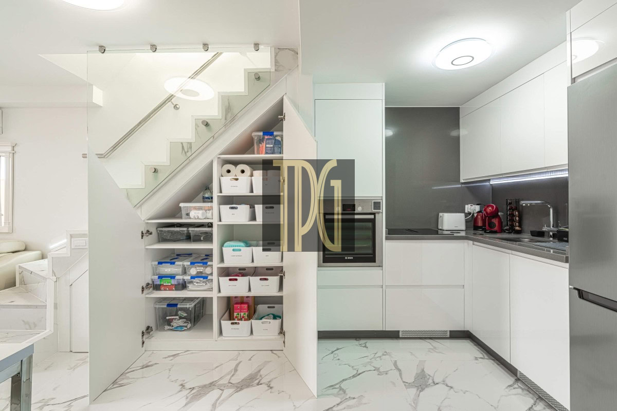 Bright, modern kitchen with white cabinets, marble floors, and a pantry under the staircase with organized bins and shelves.