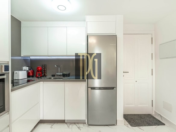 Modern white kitchen with a stainless steel fridge, built-in oven, and small appliances along a gray backsplash.