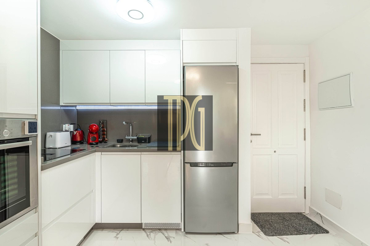 Modern white kitchen with a stainless steel fridge, built-in oven, and small appliances along a gray backsplash.