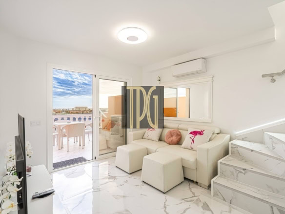 Bright white living room with marble floors, a white sofa and pink cushions, marble stairs to the right, and sliding glass doors opening to a sunny balcony.