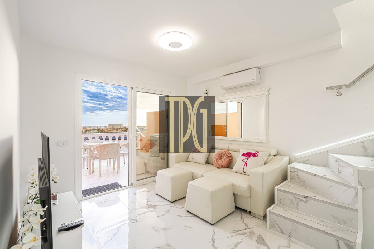 Bright white living room with marble floors, a white sofa and pink cushions, marble stairs to the right, and sliding glass doors opening to a sunny balcony.