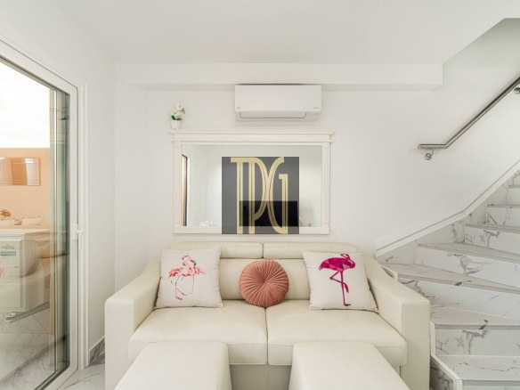 Bright, minimal living room with a white sofa, two flamingo-pattern cushions, and a pink round pillow against a white wall and marble stairs.