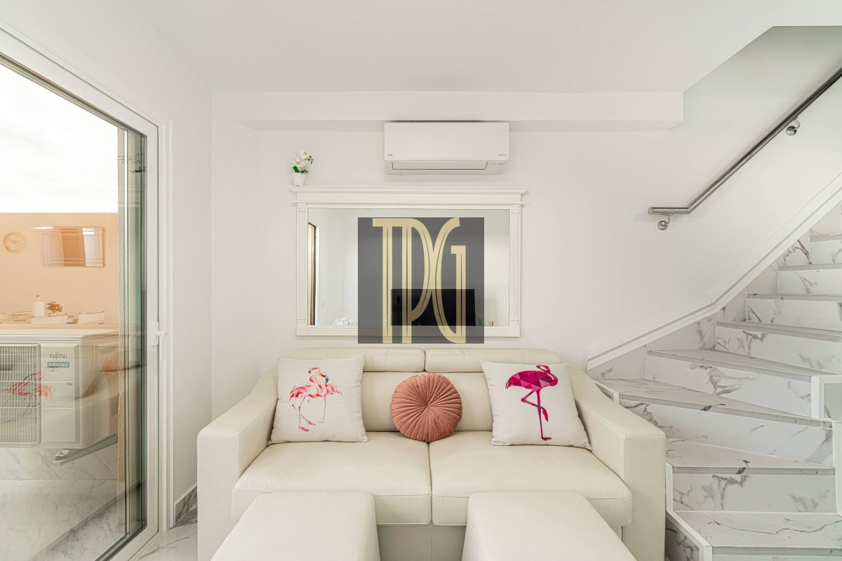 Bright, minimal living room with a white sofa, two flamingo-pattern cushions, and a pink round pillow against a white wall and marble stairs.