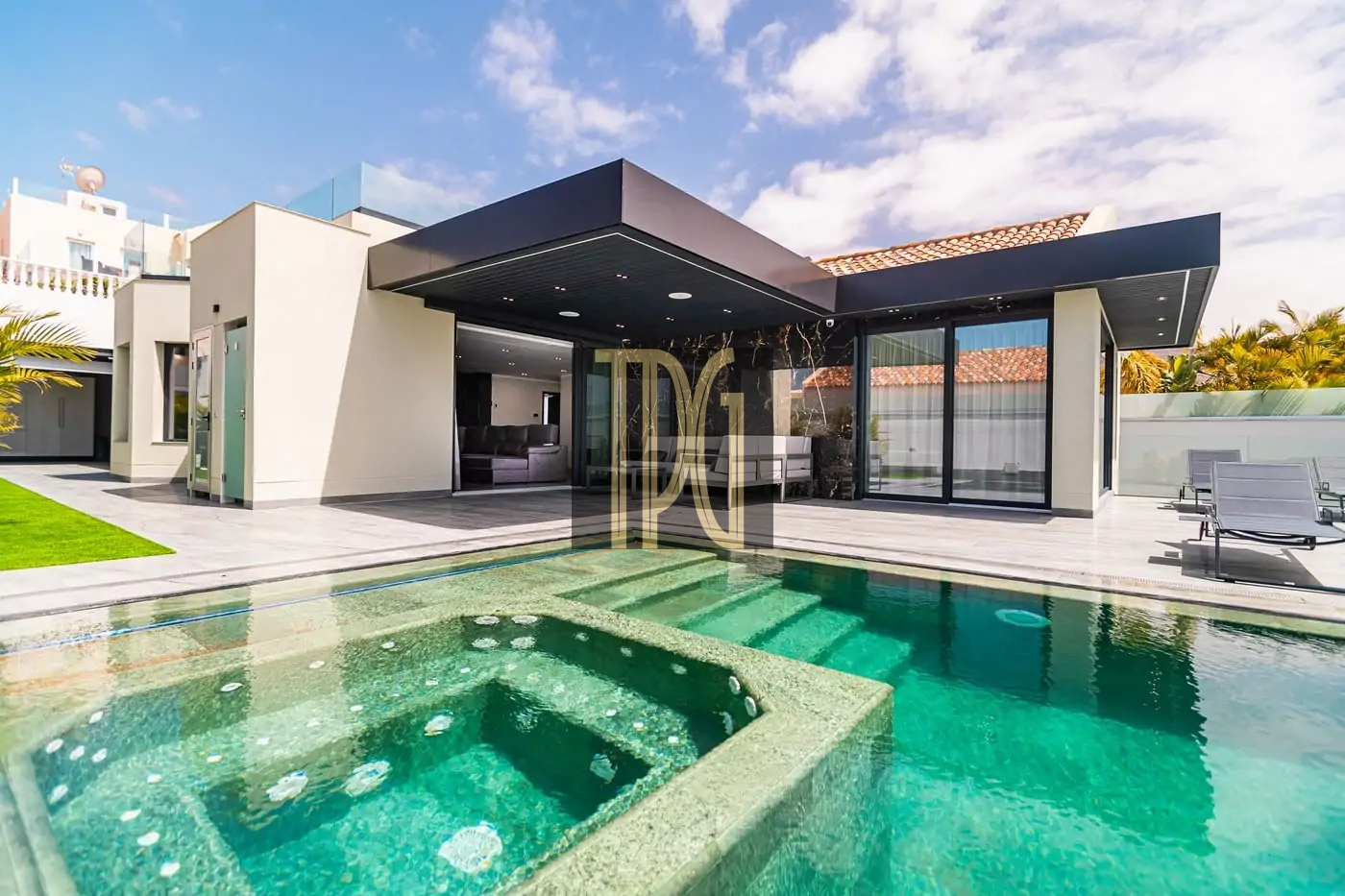 Modern single-story home with glass walls and a large turquoise swimming pool in the backyard, outdoor lounge area visible beneath a dark canopy, sunny sky above.