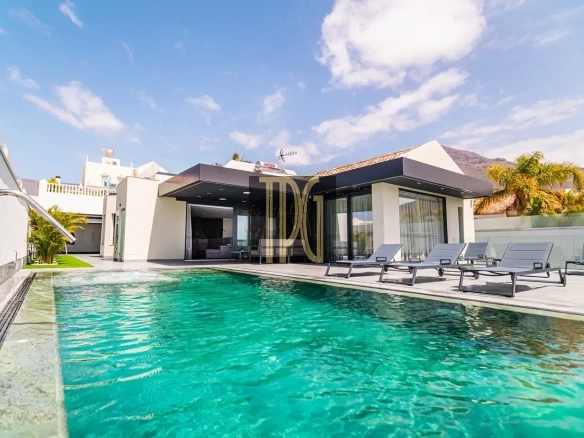 Modern villa with glass walls and a rectangular turquoise pool, white exterior, and lounge chairs on the deck.