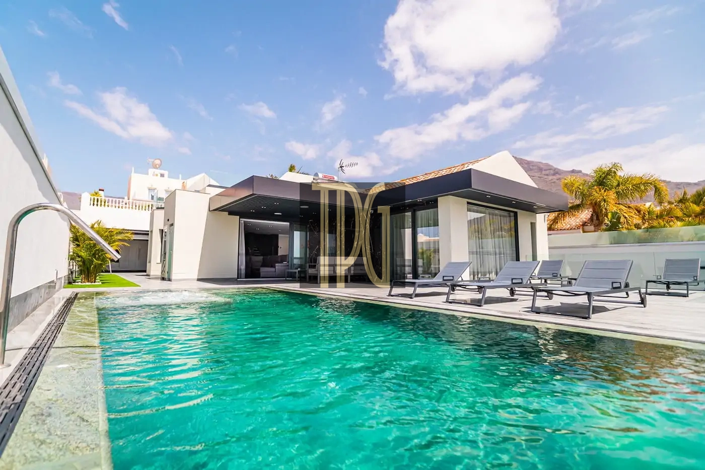 Modern villa with glass walls and a rectangular turquoise pool, white exterior, and lounge chairs on the deck.