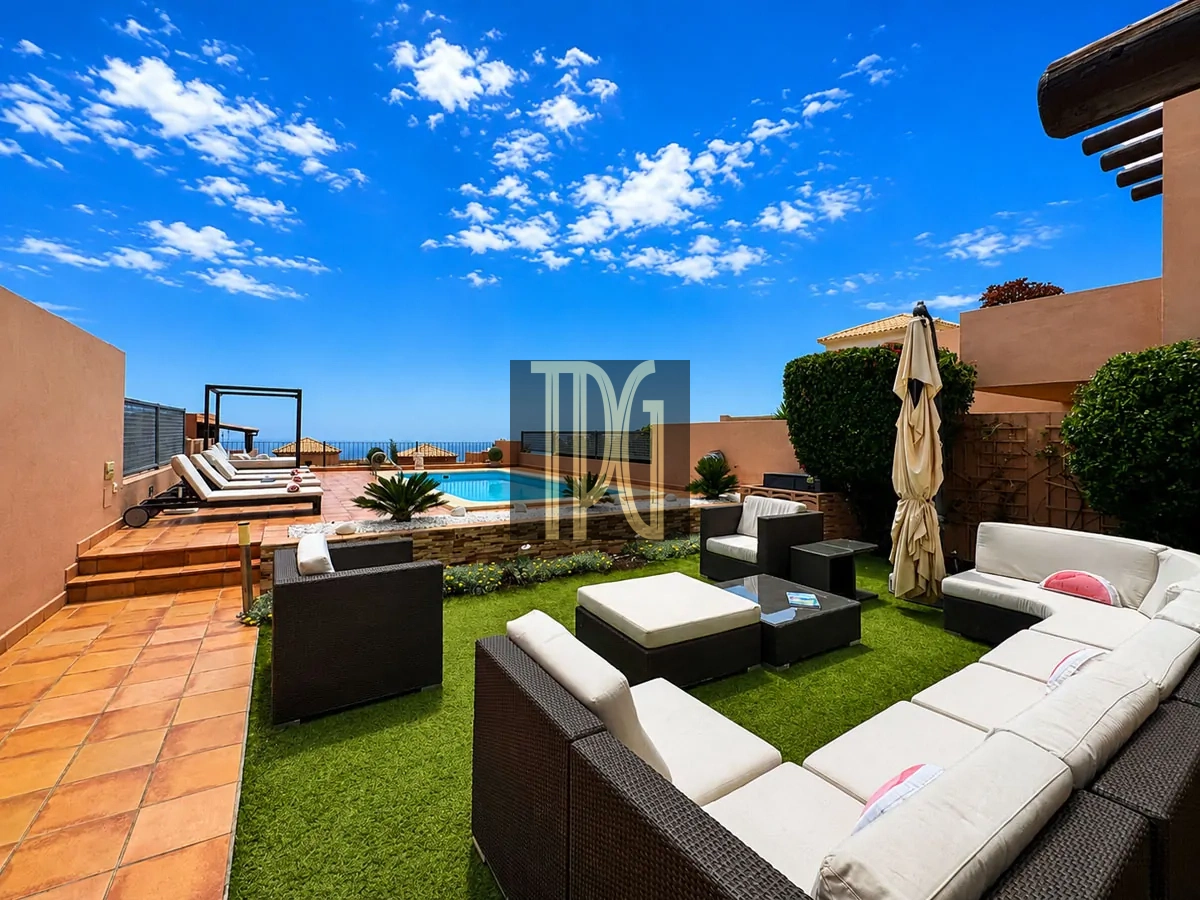 File 00002jpg Sunlit rooftop patio with a rectangular pool, tan tiled deck, and white-cushioned sectional seating under a clear blue sky.