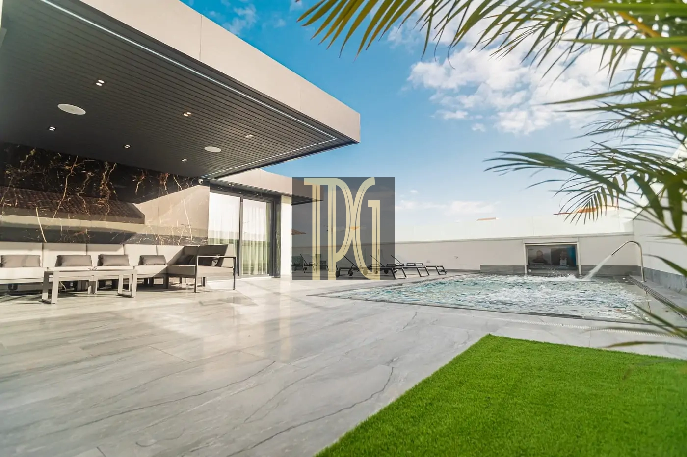 Modern upscale outdoor living area with marble patio, white cushioned seating, and a rectangular pool with lounge chairs under a covered patio, blue sky overhead and palm leaves in the foreground