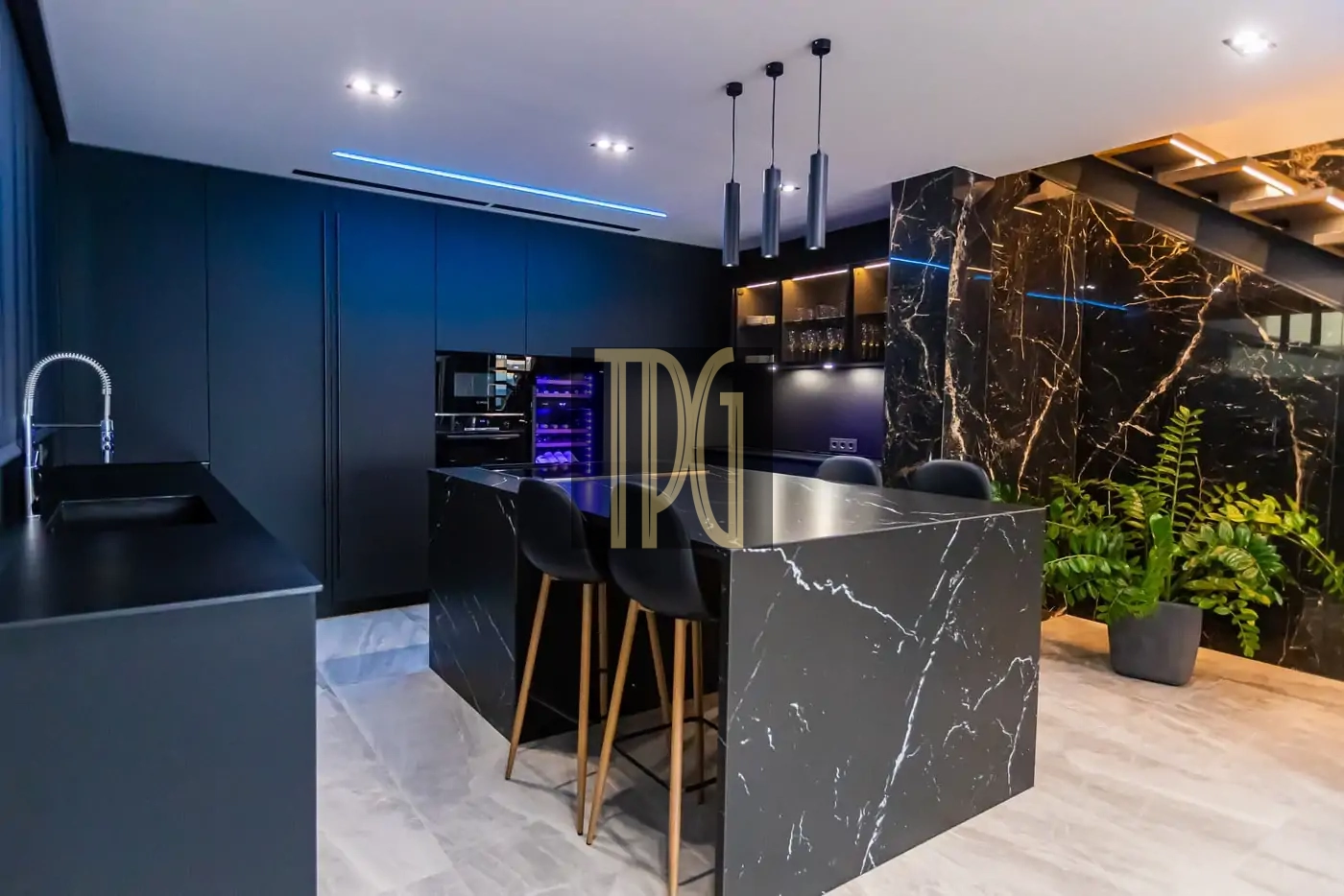 Modern dark kitchen with black marble island, three black stools, blue accent lighting, and potted plants.