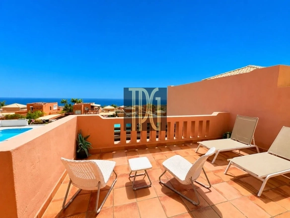 Terracotta terrace with orange walls, white lounge chairs and a small table, pool to the left and the sea beyond.