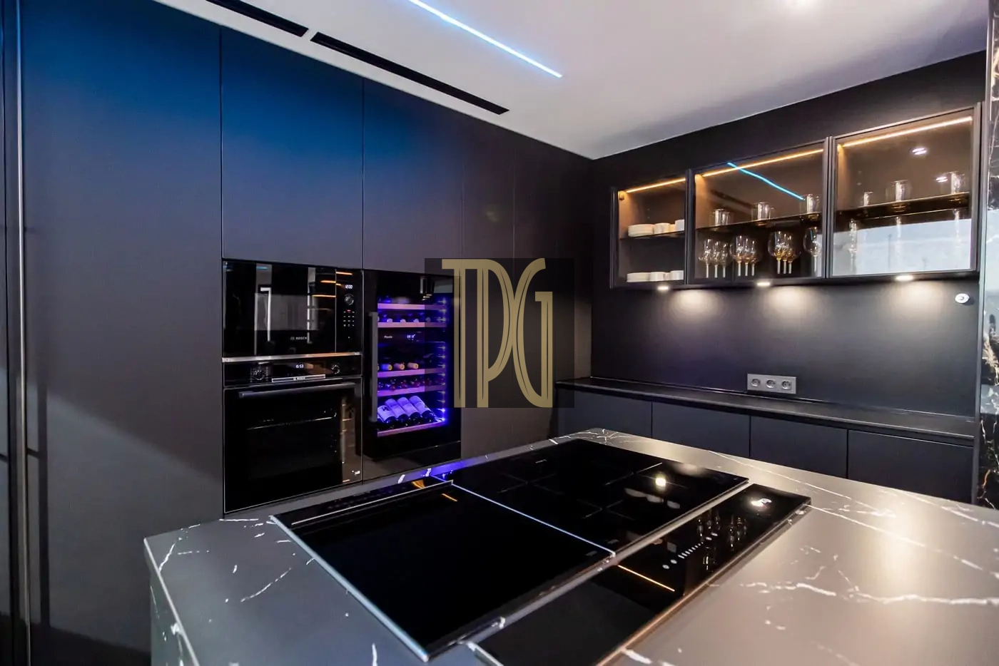 Dark modern kitchen with built-in ovens, a purple-lit wine fridge, glass-front cabinets, and a marble island with an induction cooktop.