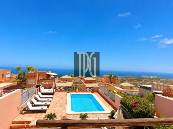 Terrace swimming pool with sun loungers and orange villas, overlooking the ocean on a sunny day.