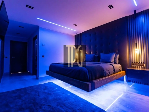 Luxurious bedroom with a low platform bed, dark upholstered headboard, blue ambient lighting and a glowing floor strip
