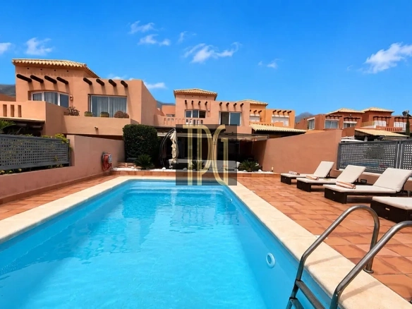 Outdoor swimming pool with terracotta patio and sun loungers on the deck under a bright blue sky at a resort.