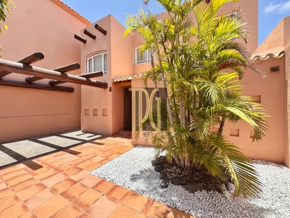Terracotta-colored building courtyard with a tall palm tree in a white pebble bed and terracotta floor tiles, left side features wooden beams.