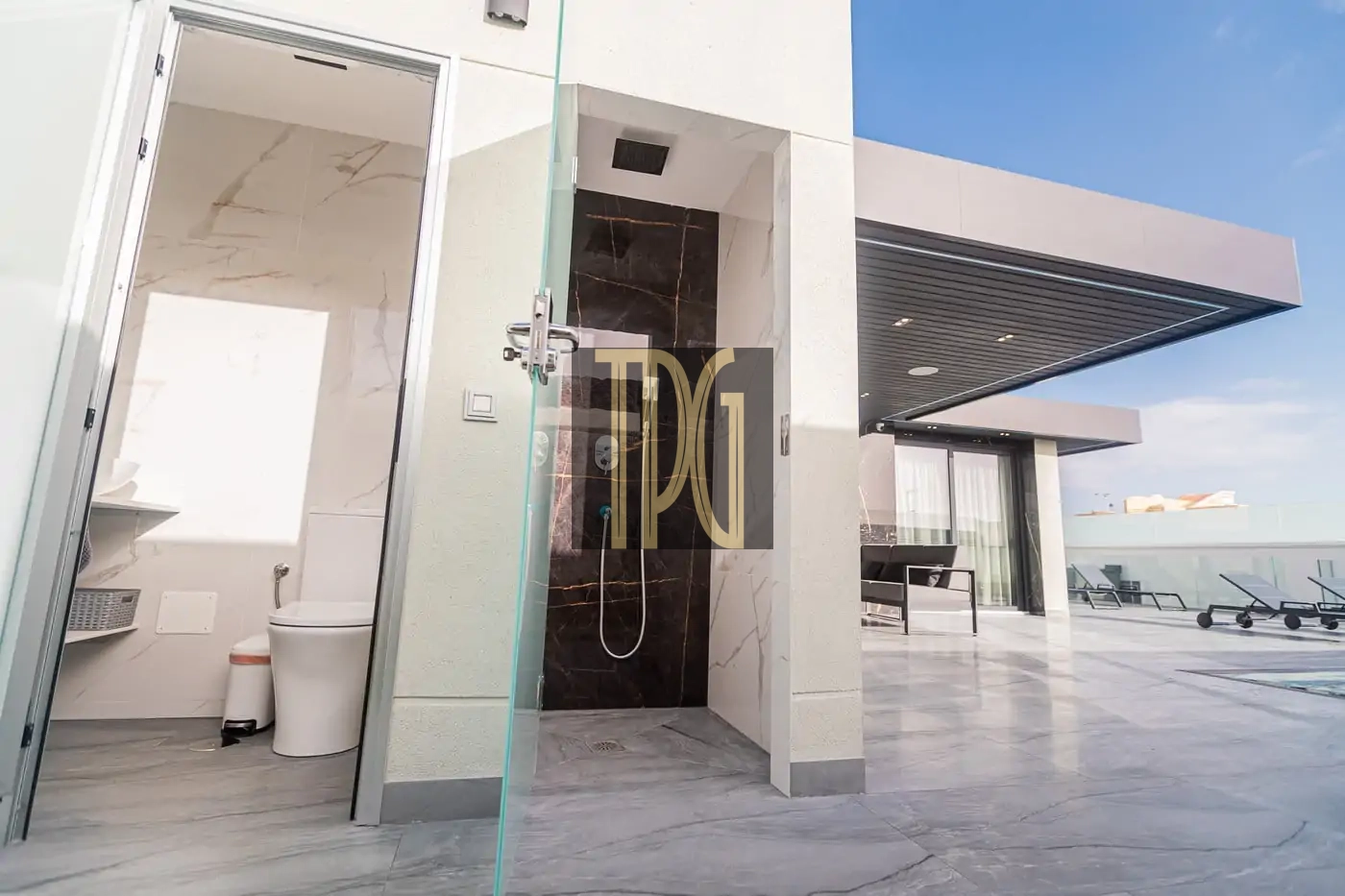 Modern rooftop terrace with a glass-enclosed outdoor shower, an adjacent bathroom, and sun loungers on a marble-tiled deck.